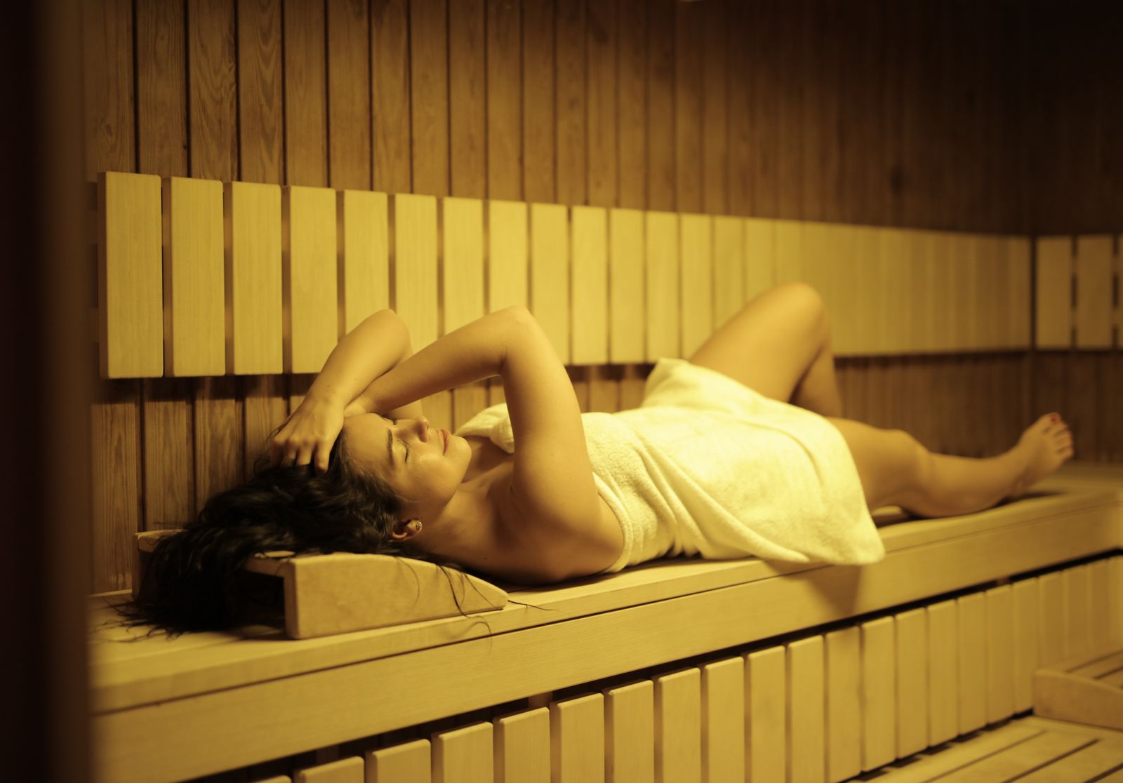 Inside the Moroccan Hammam Ritual at Kimantra: A Step-by-Step Photo Story 4 Woman wrapped in a white towel reclining on a warm wooden bench in soft golden light