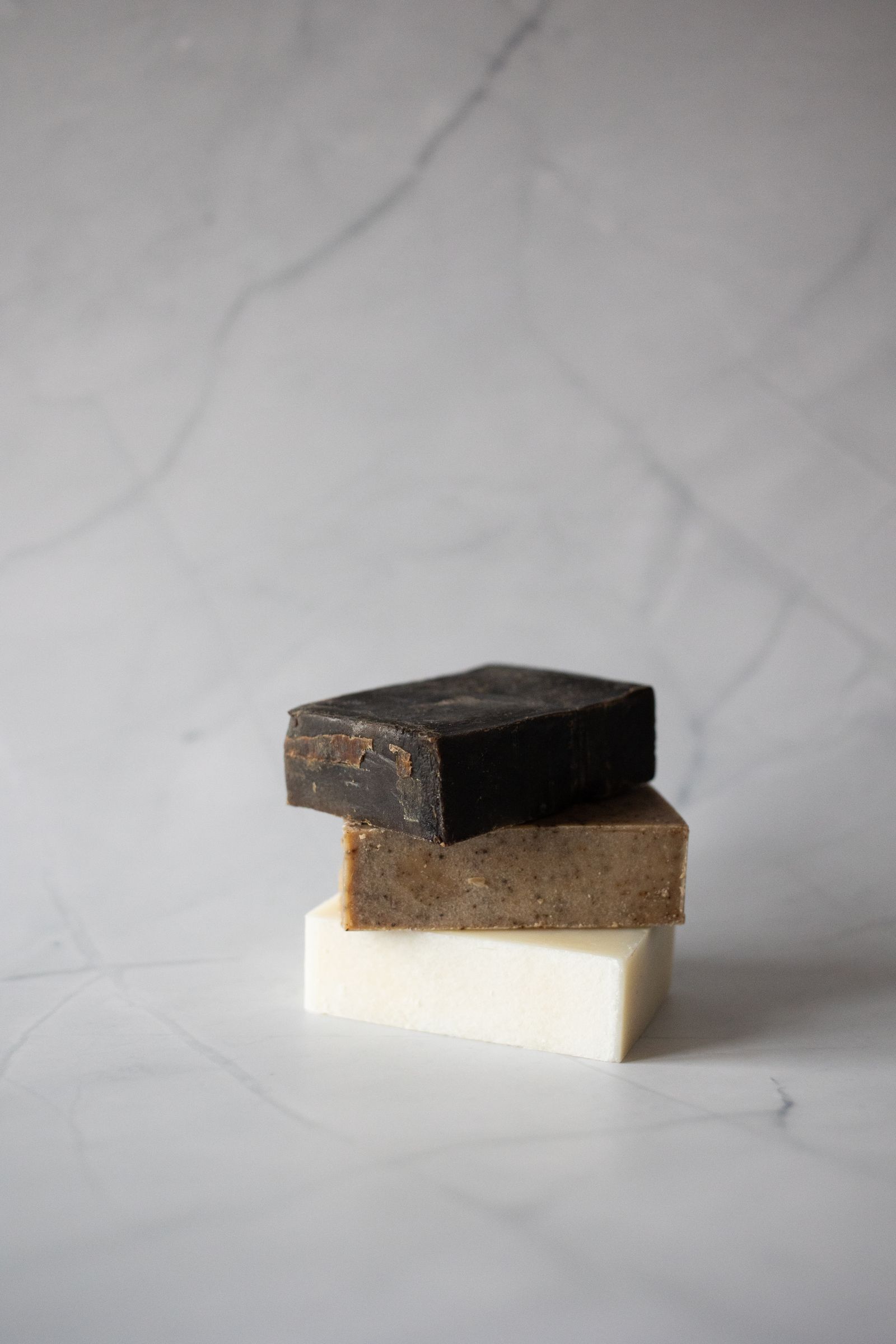 Inside the Moroccan Hammam Ritual at Kimantra: A Step-by-Step Photo Story 5 Stack of three artisan soap blocks, the top one a dark olive-black, resting on grey marble