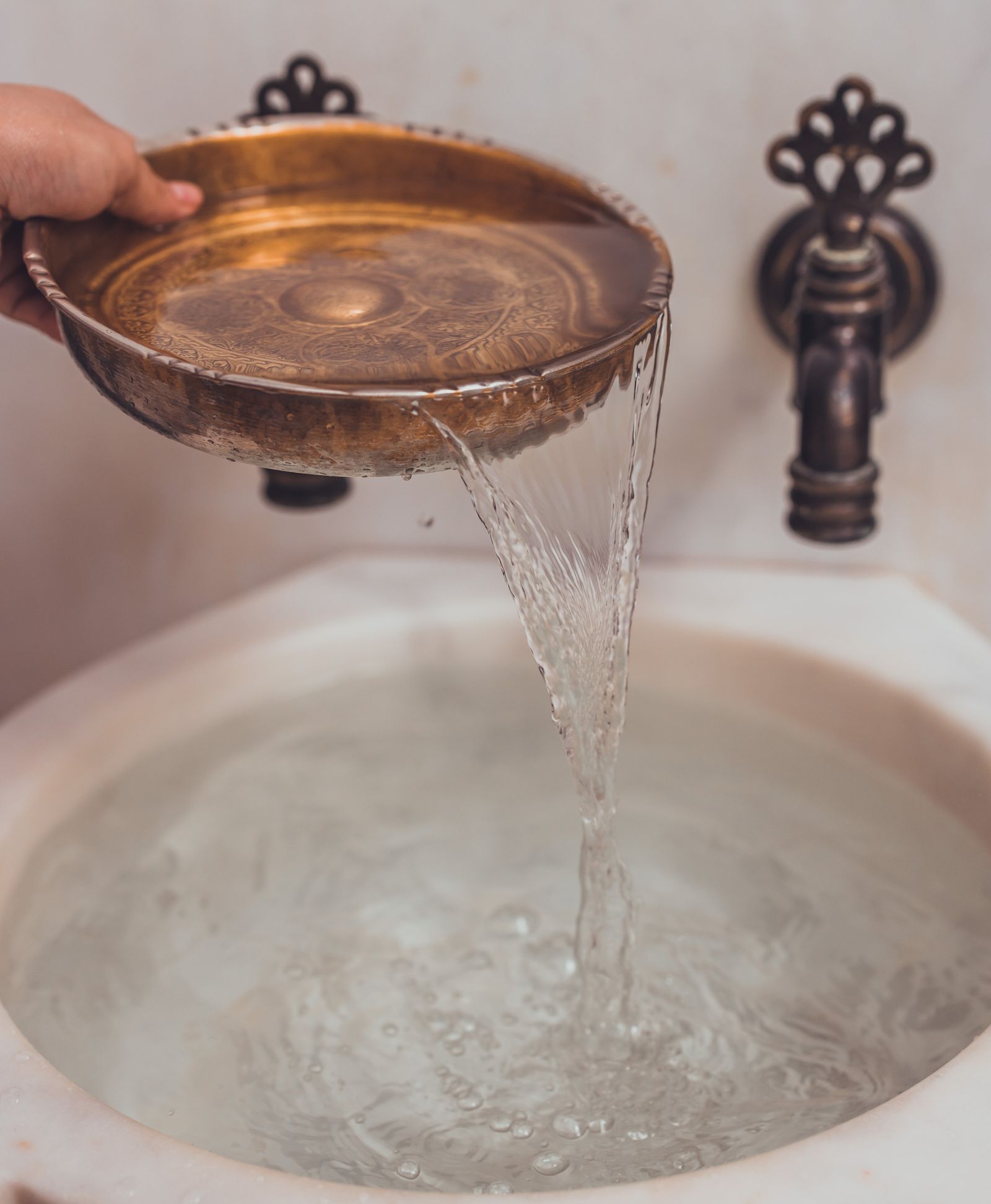 Inside the Moroccan Hammam Ritual at Kimantra: A Step-by-Step Photo Story 10 Engraved brass hammam bowl pouring water into a marble kurna basin with an ornate brass tap
